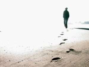 Mann hinterlässt am Sandstrand Fußspuren und geht in die unerkenntliche Ferne als Symbol für das spirituelle Lehrwerk "Ein Kurs in Wundern"